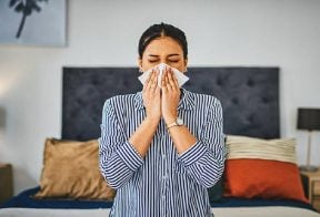 Woman blows her nose into a tissue in her bedroom